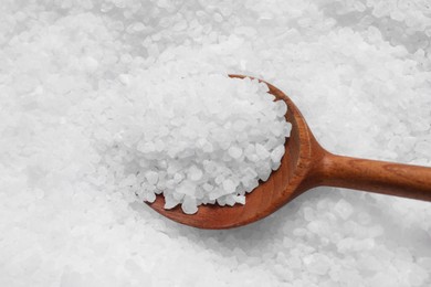 Photo of Pile of natural sea salt with wooden spoon, closeup