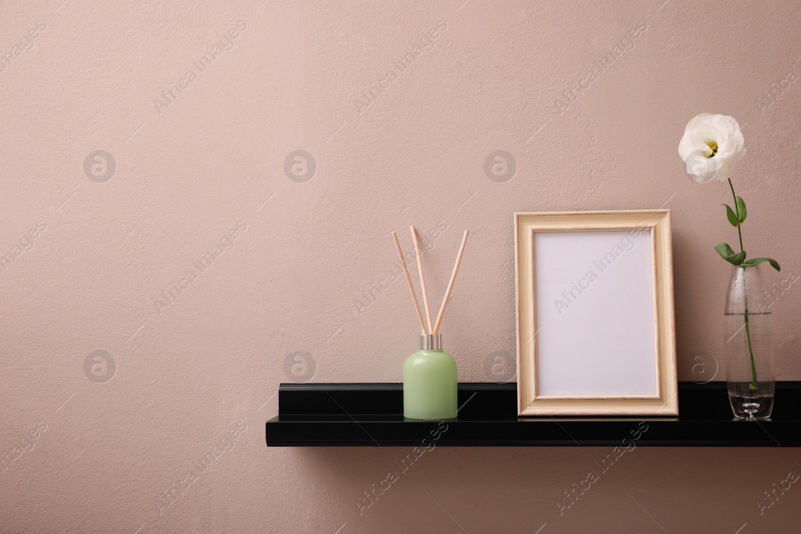 Photo of Empty photo frame, air reed freshener and beautiful flower on shelf near pink wall, space for text
