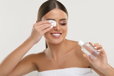 Photo of Beautiful woman removing makeup with cotton pad on light grey background