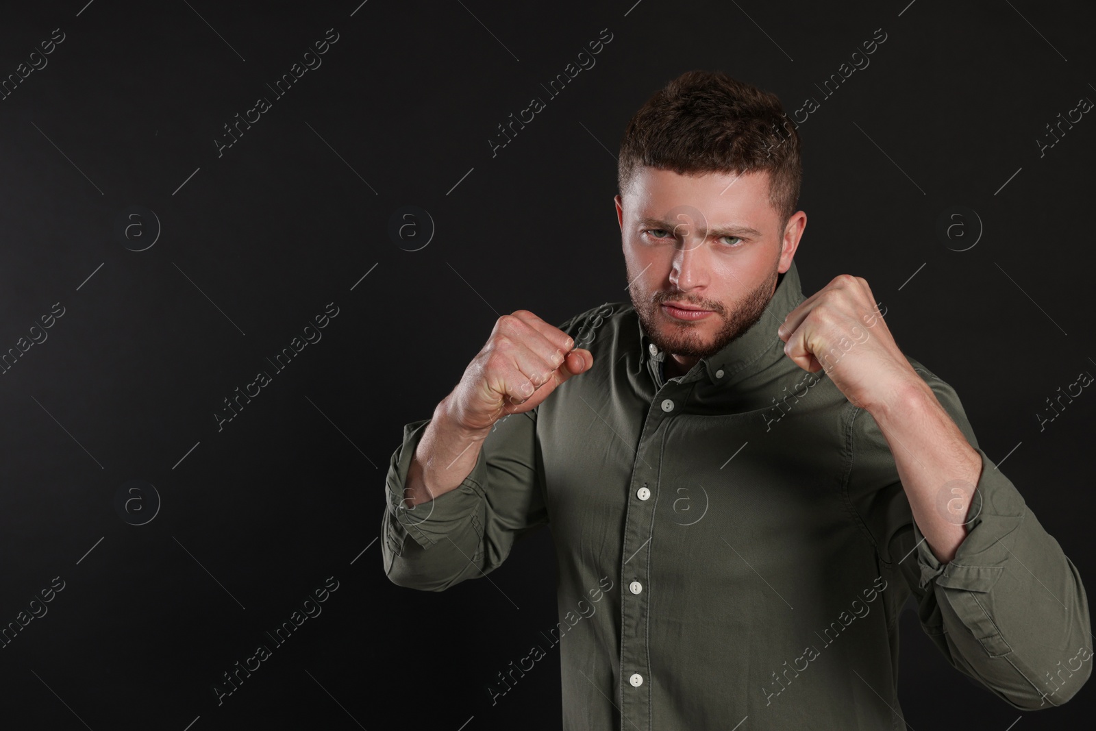 Photo of Young man ready to fight on black background, space for text