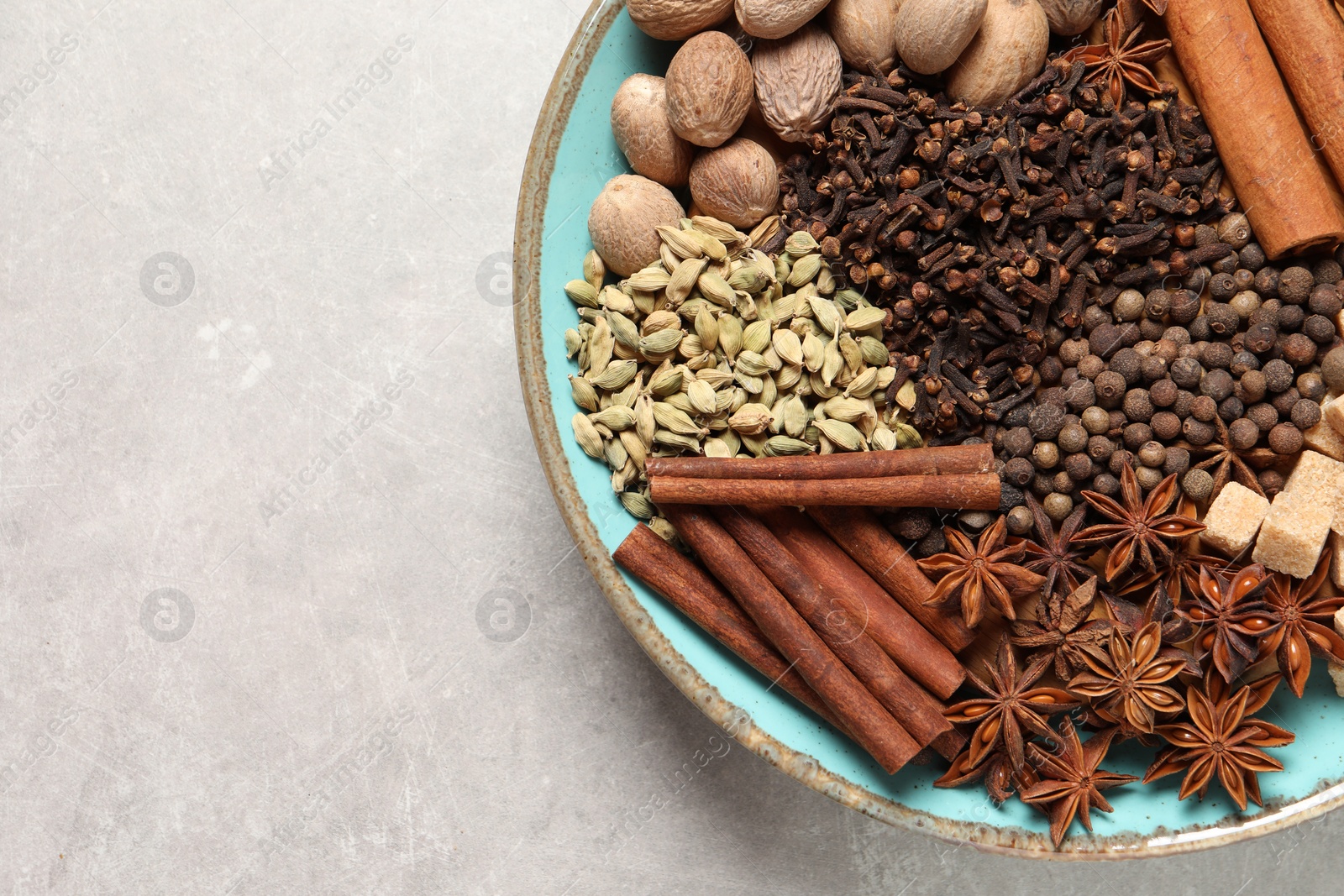 Photo of Different spices and nuts in bowl on light gray textured table, top view. Space for text