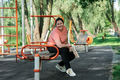 Overweight woman with towel sitting on bench of sports ground