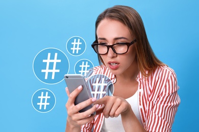 Image of Young woman using modern smartphone on light blue background. Hashtag symbols near device