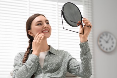 Young woman looking at her new dental implants in mirror indoors