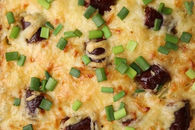 Photo of Tasty sausage casserole with green onions as background, top view