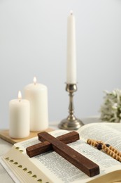 Church candles, wooden cross, rosary beads and Bible on table, closeup