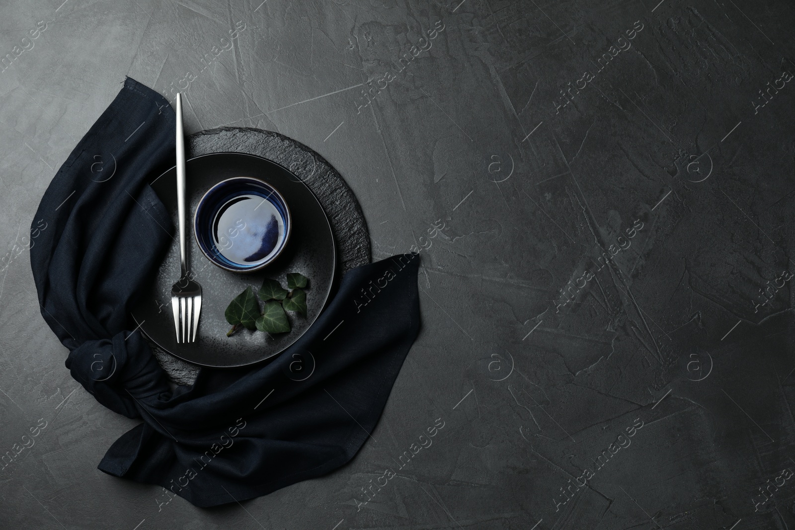 Photo of Stylish table setting. Dishes, fork, napkin and green leaves on grey surface, top view with space for text