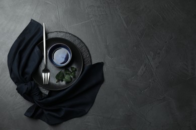 Photo of Stylish table setting. Dishes, fork, napkin and green leaves on grey surface, top view with space for text
