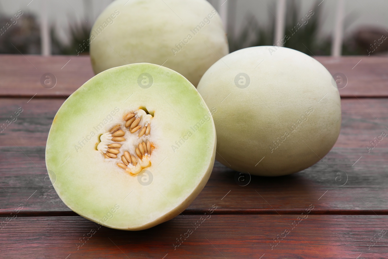 Photo of Whole and cut fresh ripe melons on wooden table outdoors