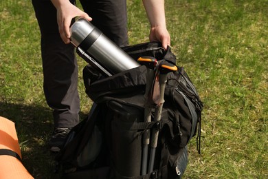 Hiker putting thermos into backpack outdoors, closeup
