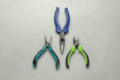 Different pliers on grey textured table, flat lay