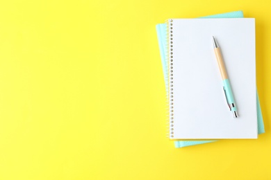 Photo of Notebooks and pen on yellow background, top view. Space for text