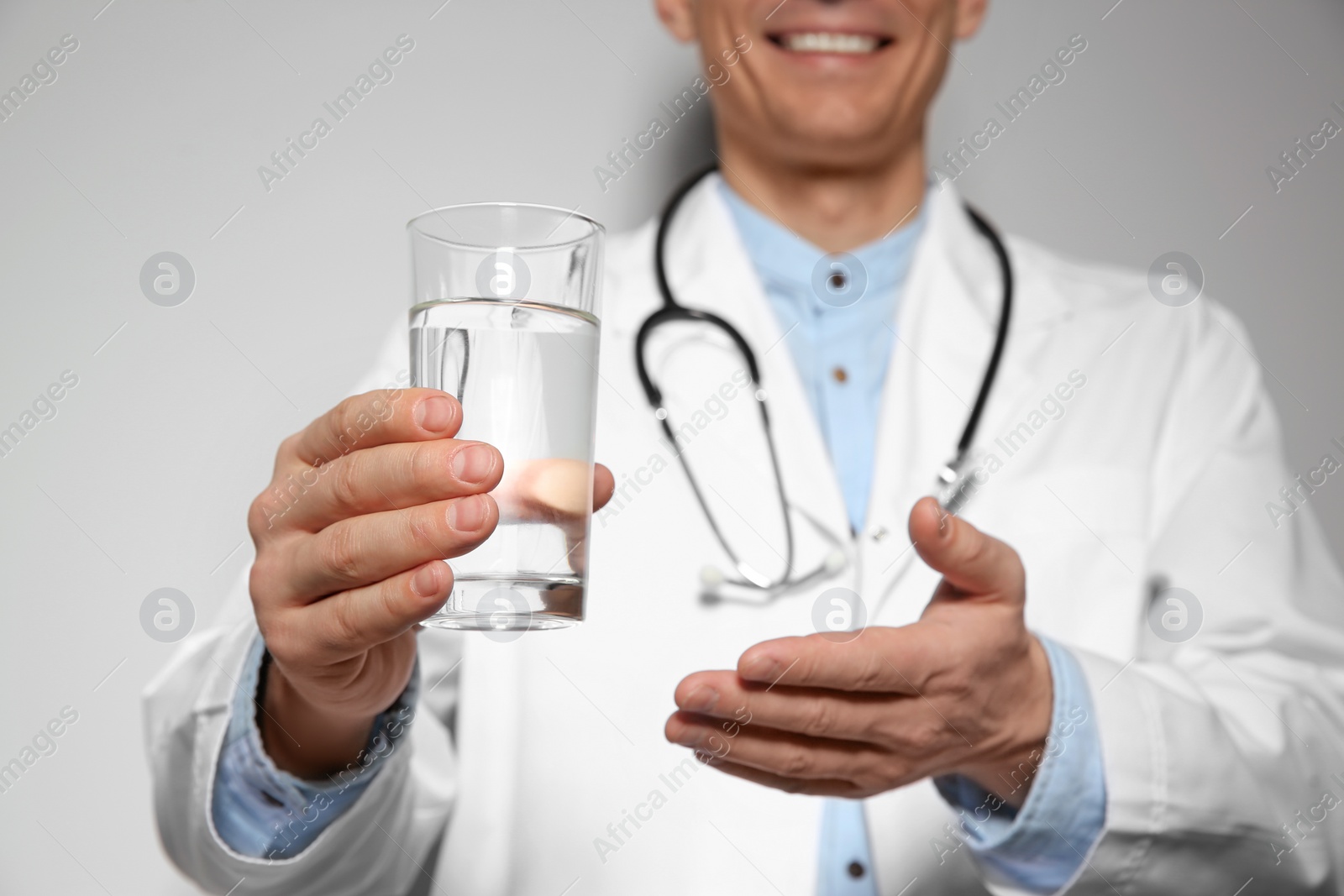 Photo of Nutritionist holding glass of pure water on light grey background, focus on hand