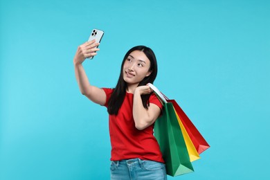 Photo of Smiling woman with shopping bags taking selfie on light blue background