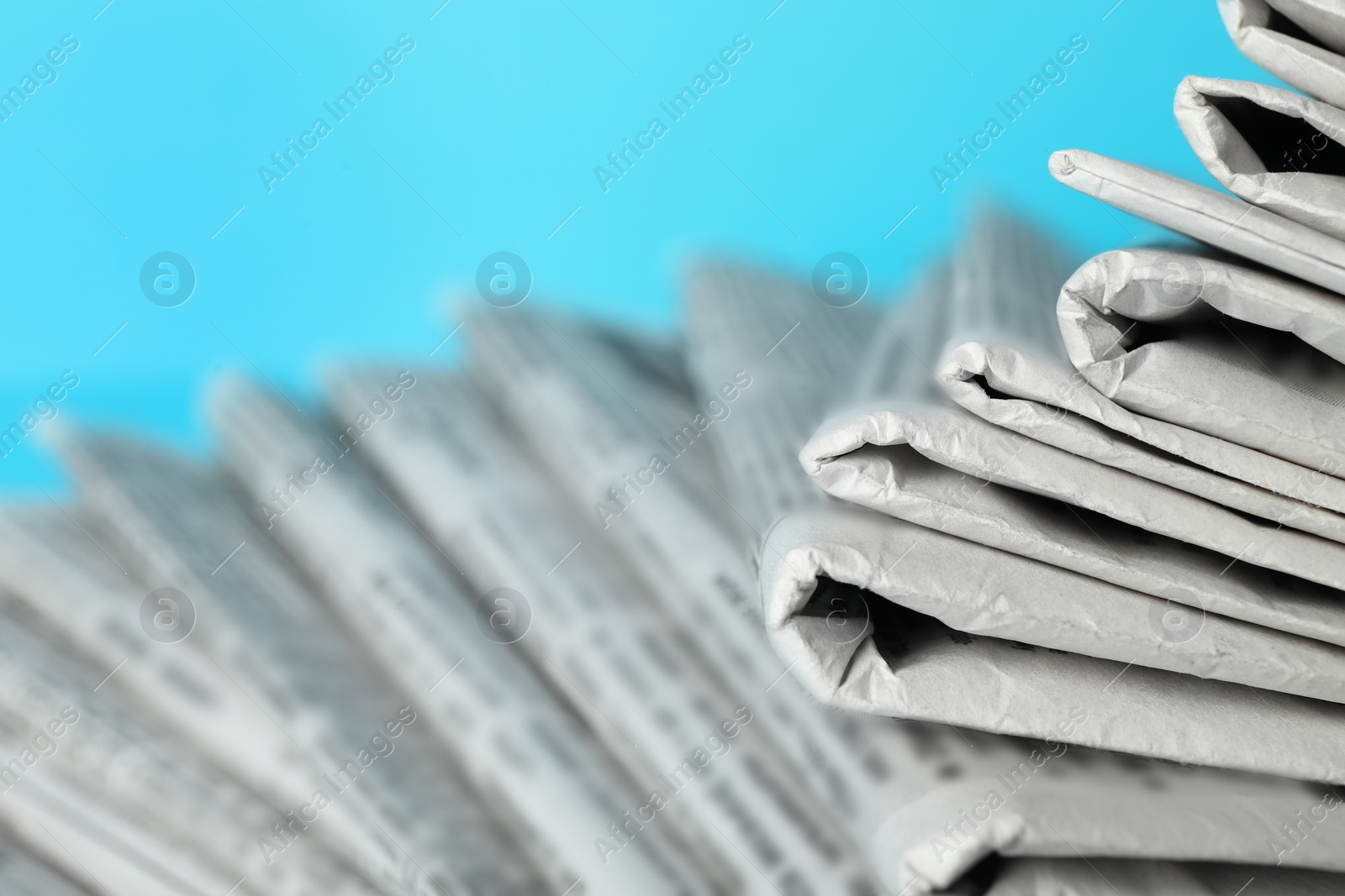 Photo of Stack of newspapers on light blue background, closeup. Journalist's work