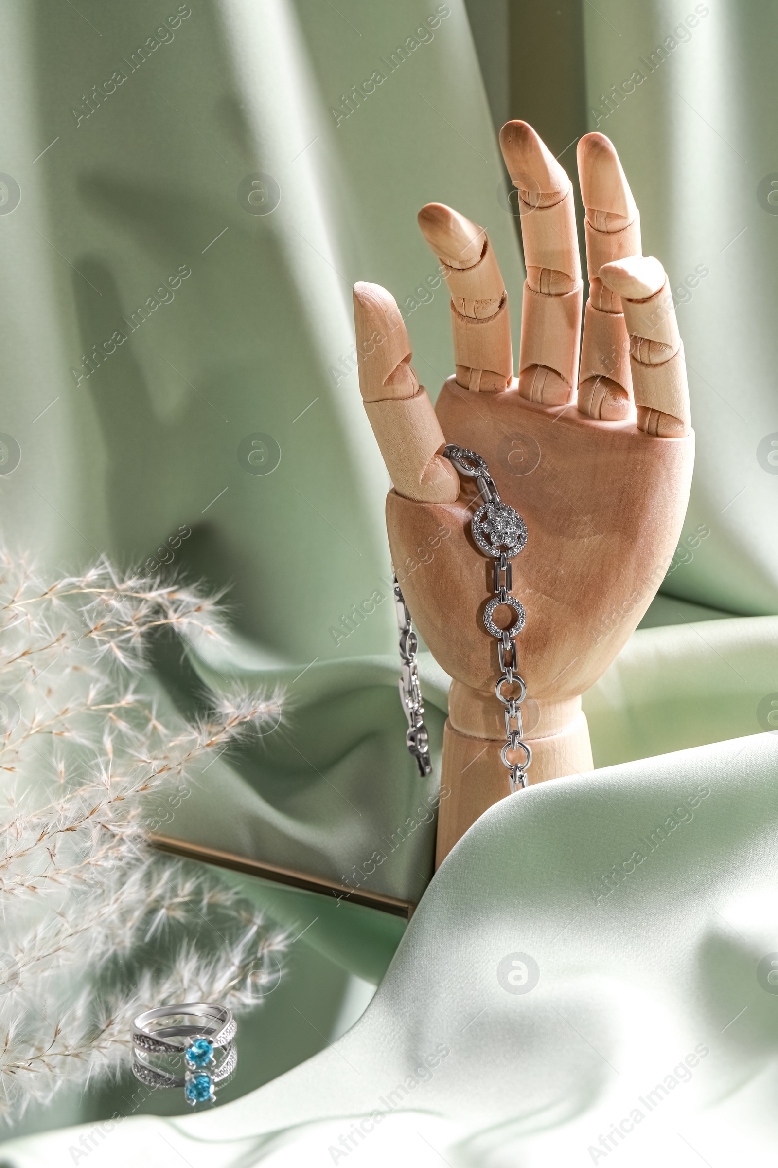 Photo of Elegant jewelry. Wooden mannequin hand with luxury bracelet and rings on green cloth