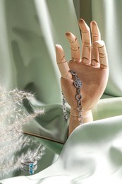 Photo of Elegant jewelry. Wooden mannequin hand with luxury bracelet and rings on green cloth