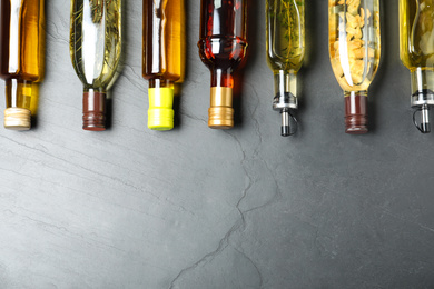 Photo of Different sorts of cooking oil in bottles on grey table, flat lay. Space for text