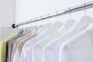 Photo of Rack with different stylish shirts near white wall, closeup. Organizing clothes