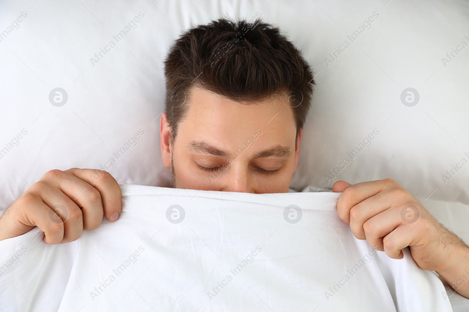 Photo of Handsome man covering his face with blanket while lying on pillow, top view. Bedtime