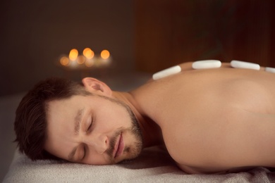 Photo of Handsome man receiving hot stone massage in spa salon