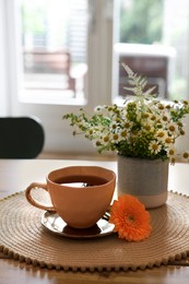 Cup of delicious chamomile tea and fresh flowers on wooden table in room