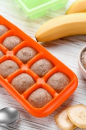 Photo of Banana puree in ice cube tray with ingredients on white wooden table