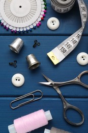 Photo of Flat lay composition with thimbles and different sewing tools on blue wooden table