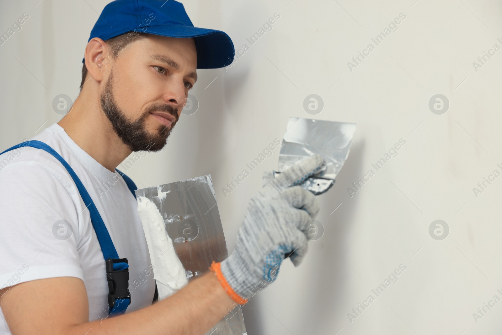 Photo of Professional worker plastering wall with putty knives indoors