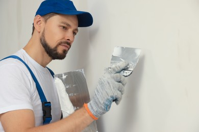 Photo of Professional worker plastering wall with putty knives indoors