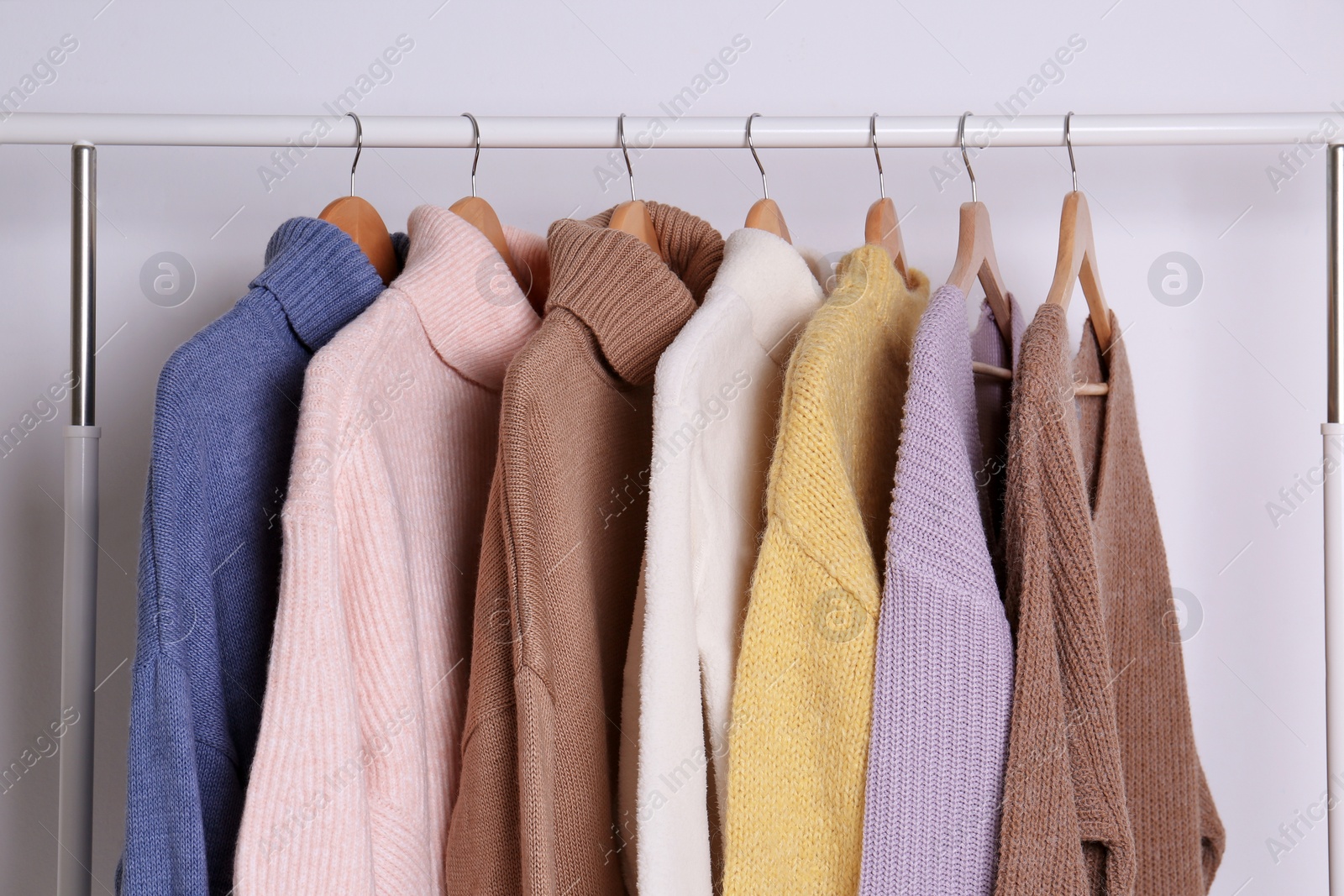 Photo of Warm sweaters hanging on rack against white background