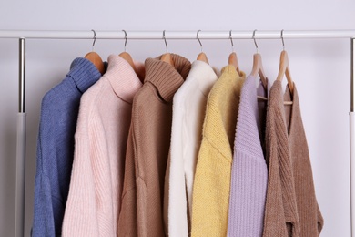 Warm sweaters hanging on rack against white background