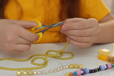 Girl making beaded jewelry at white wooden table, closeup