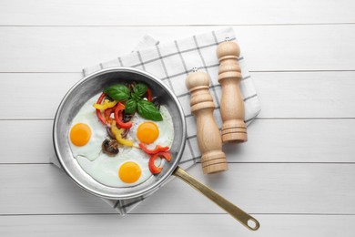 Tasty fried eggs with vegetables in pan and spice shakers on white wooden table, flat lay