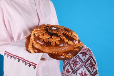 Photo of Woman with korovai on light blue background, closeup. Ukrainian bread and salt welcoming tradition