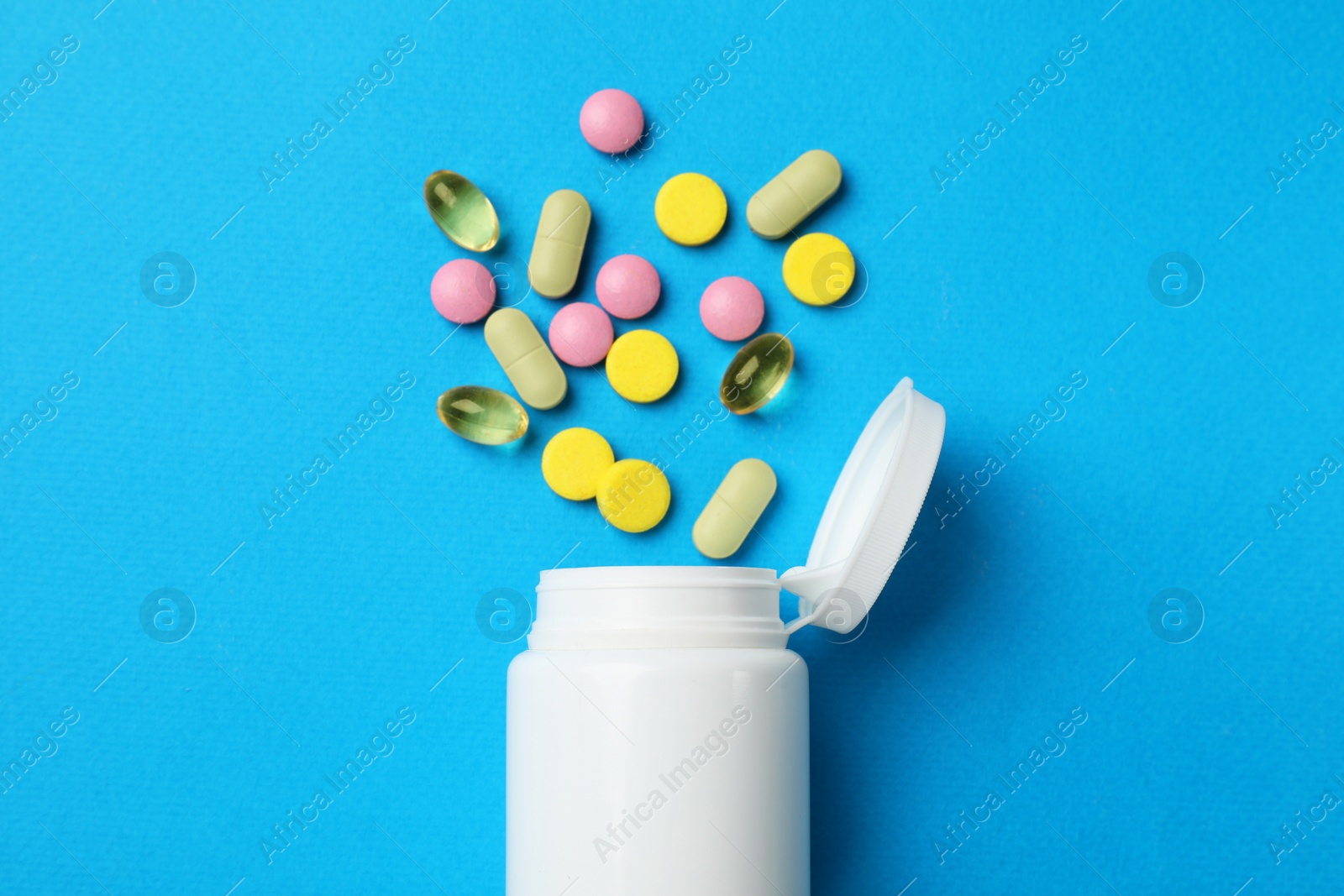 Photo of Different vitamin pills and bottle on light blue background, top view