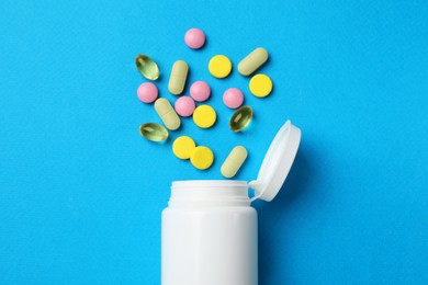 Different vitamin pills and bottle on light blue background, top view