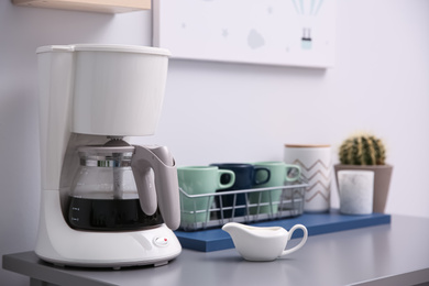 Photo of Modern coffeemaker and dishware on grey table in kitchen