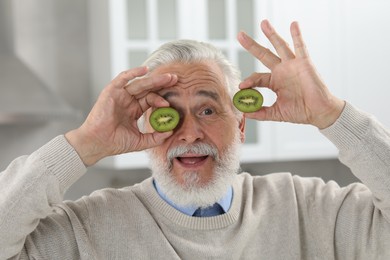Photo of Senior man holding halves of kiwi indoors