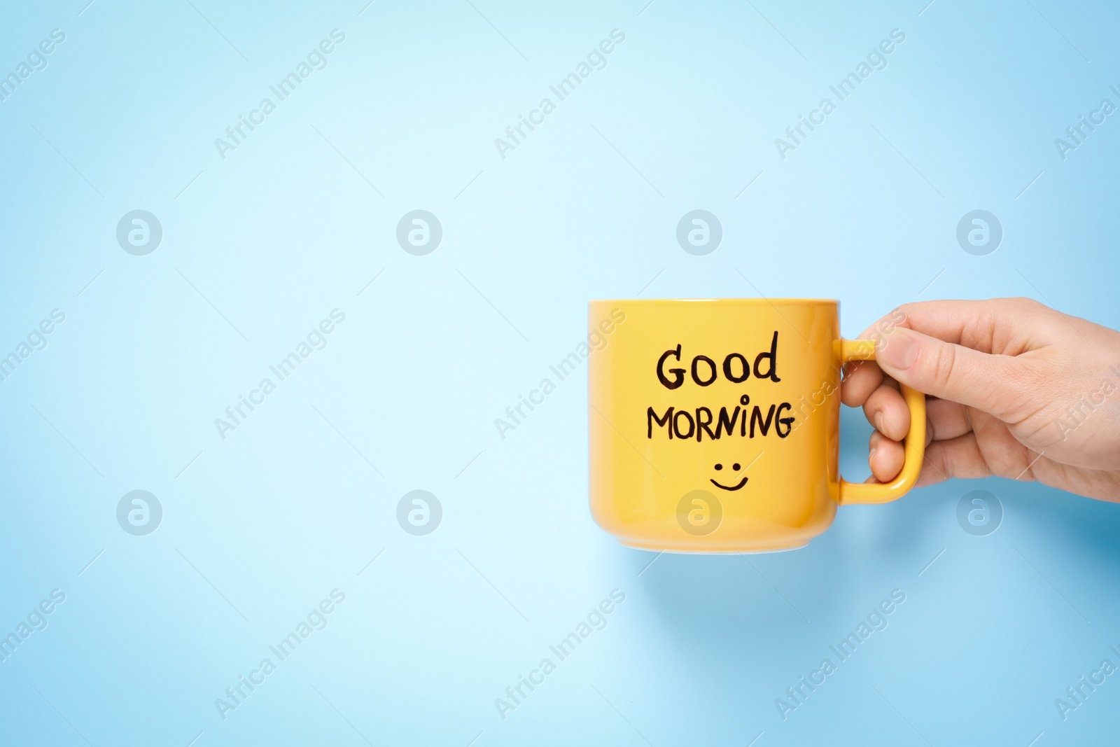 Photo of Woman holding cup of coffee with words GOOD MORNING on light blue background, closeup. Space for text