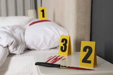Bloody knife and crime scene markers on nightstand in bedroom