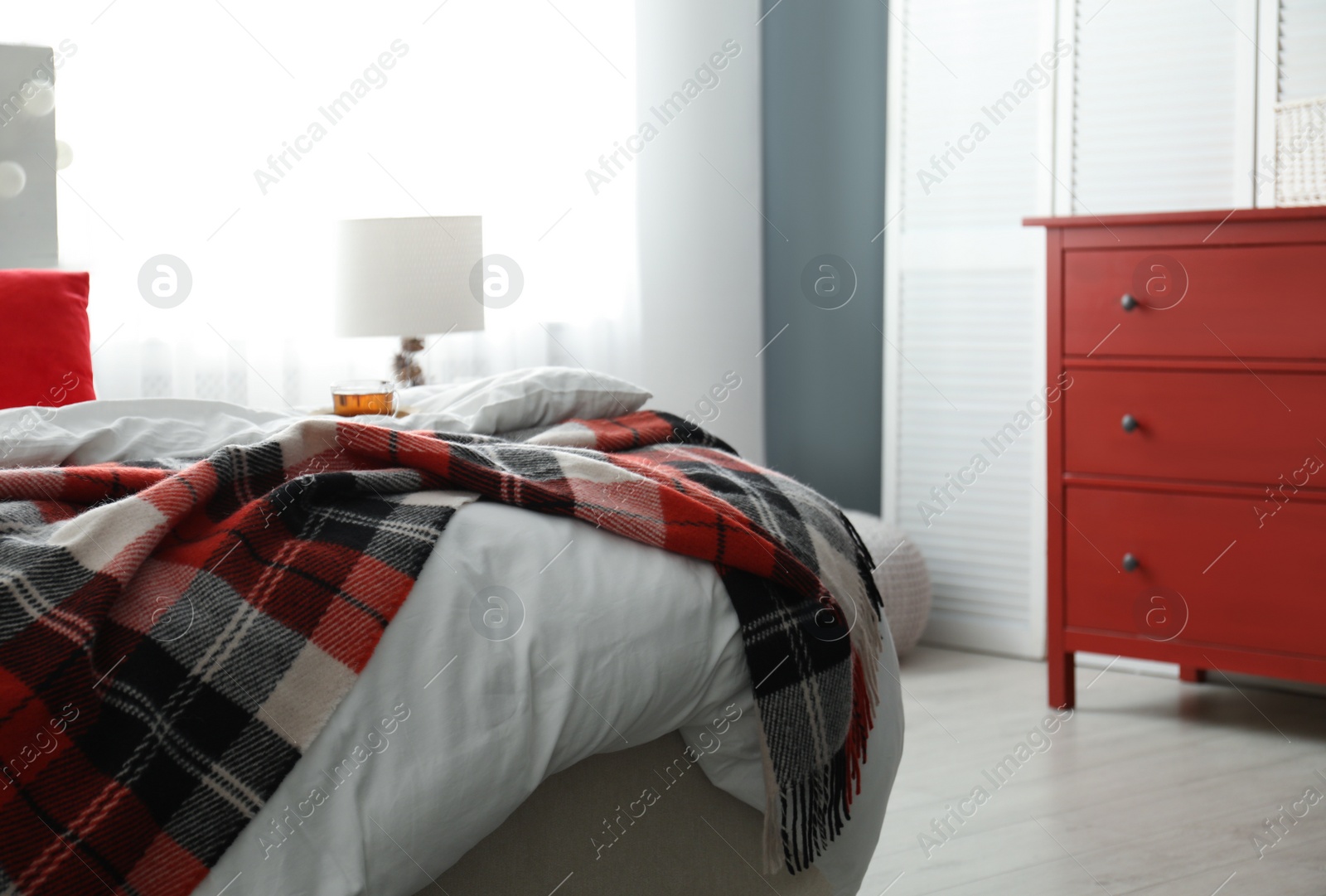 Photo of Comfortable bed with warm checkered plaid in stylish room interior