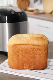 Photo of Breadmaker and fresh homemade bread on wooden table in kitchen