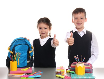 Photo of Cute children at table with school stationery on white background