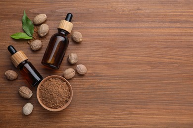 Photo of Bottles of nutmeg oil, nuts and powder on wooden table, flat lay. Space for text