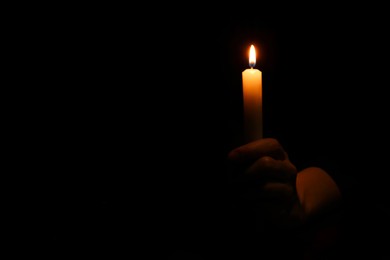 Photo of Woman holding burning candle in hand on black background, closeup. Space for text