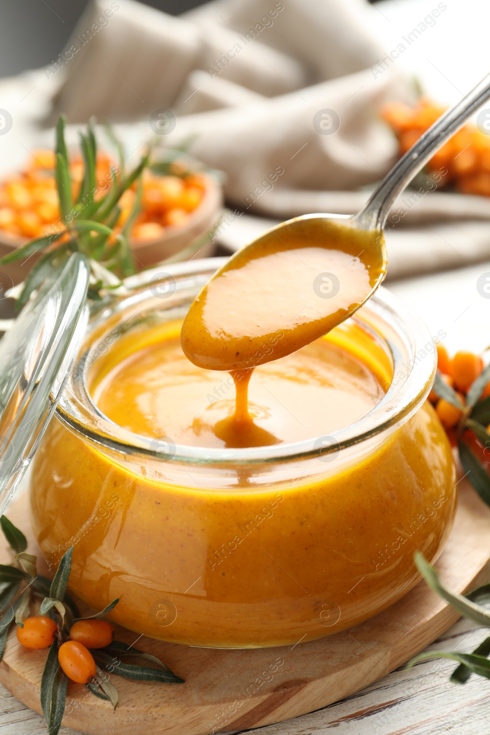 Photo of Spoon with delicious sea buckthorn jam over jar on table, closeup