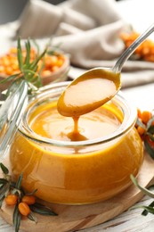 Photo of Spoon with delicious sea buckthorn jam over jar on table, closeup