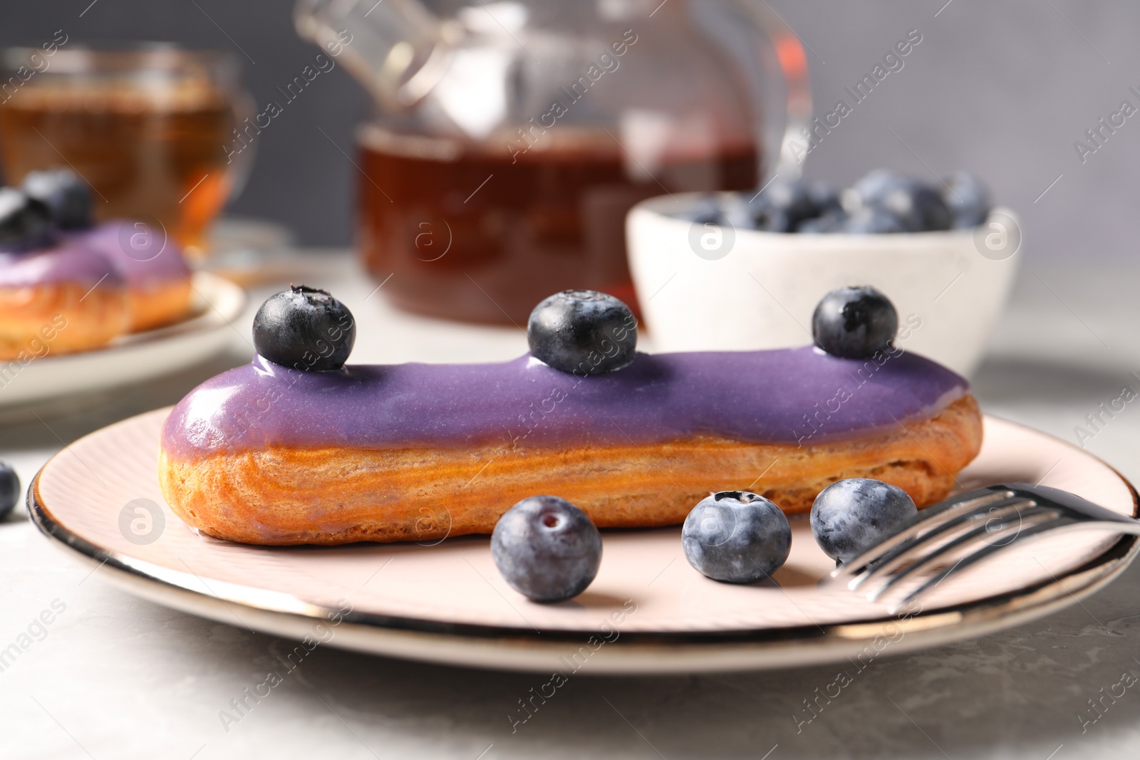 Photo of Tasty glazed eclair with blueberries on grey marble table, closeup