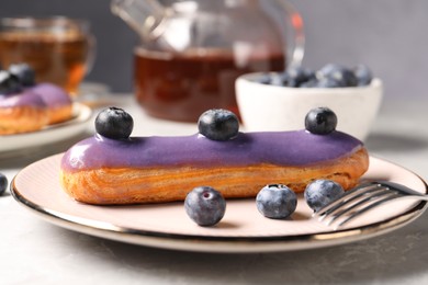 Tasty glazed eclair with blueberries on grey marble table, closeup